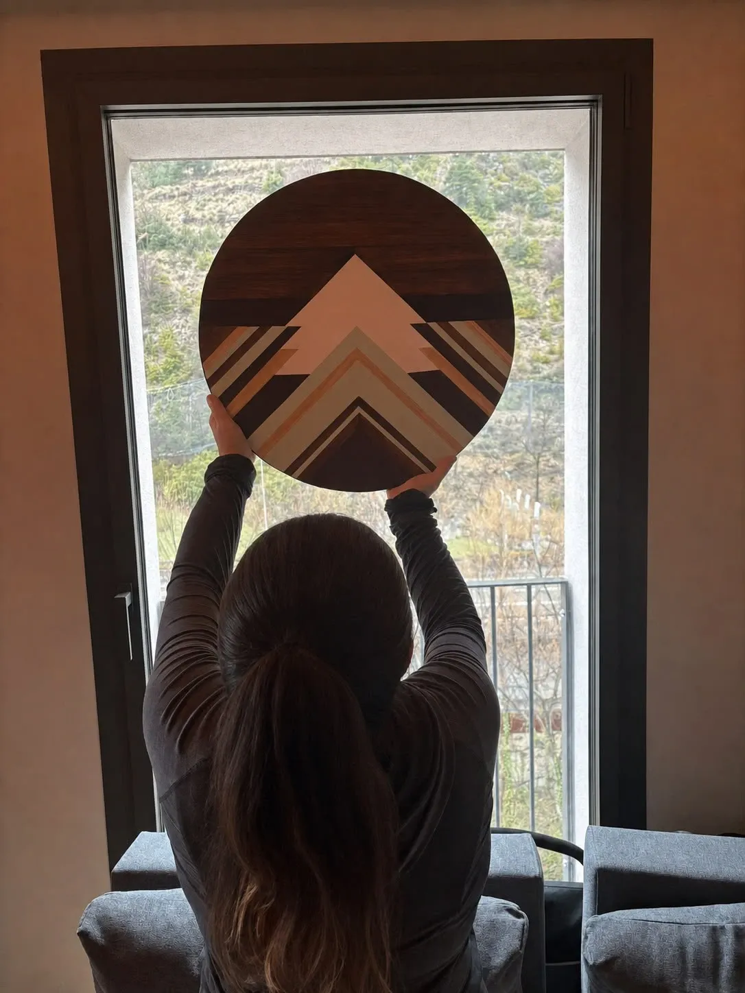 Maribel Weber sosteniendo una pieza circular de madera frente a una ventana